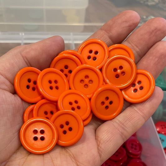 Hand holding orange buttons with a container of colorful buttons in the background