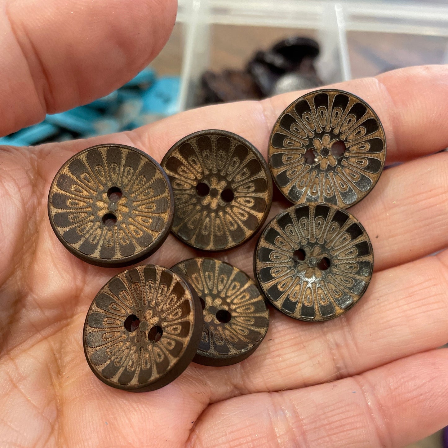 Hand holding six bronze buttons with intricate designs.