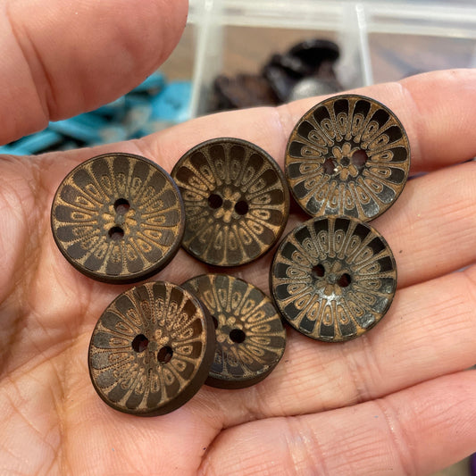 Hand holding six bronze buttons with intricate designs.