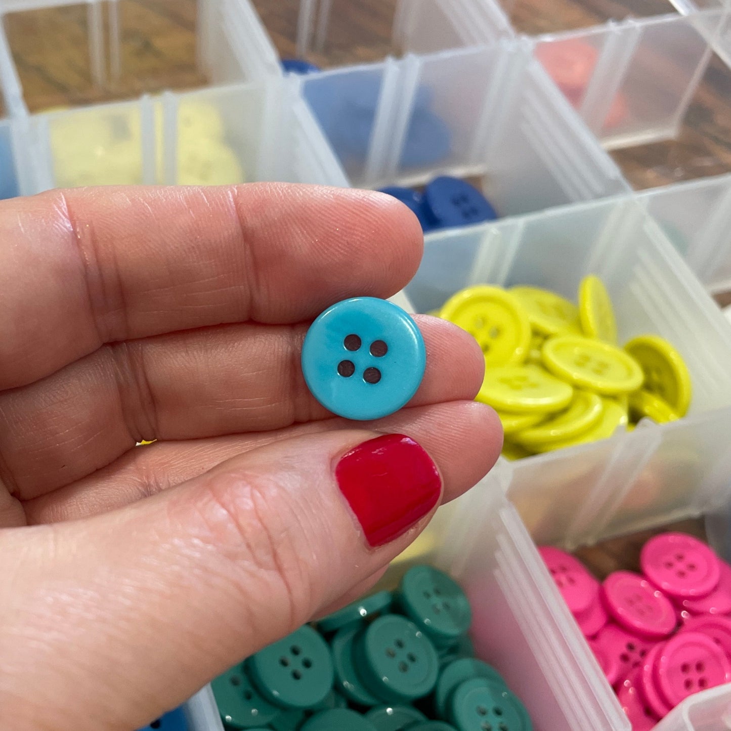 Hand holding a blue button with a container of colorful buttons in the background