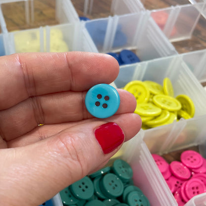 Hand holding a blue button with a container of colorful buttons in the background