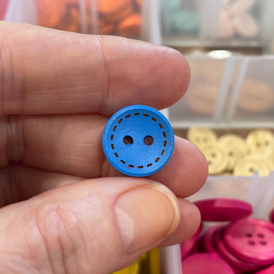 Hand holding a blue button with a container of colorful buttons in the background