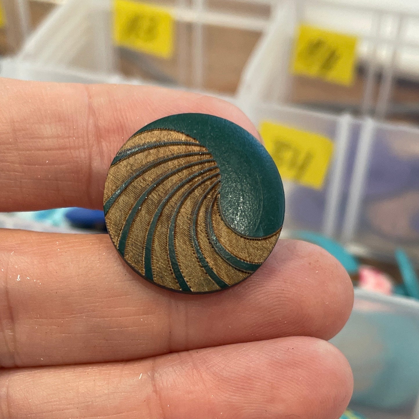 Hand holding a decorative button with a detailed pattern, surrounded by various buttons in the background.
