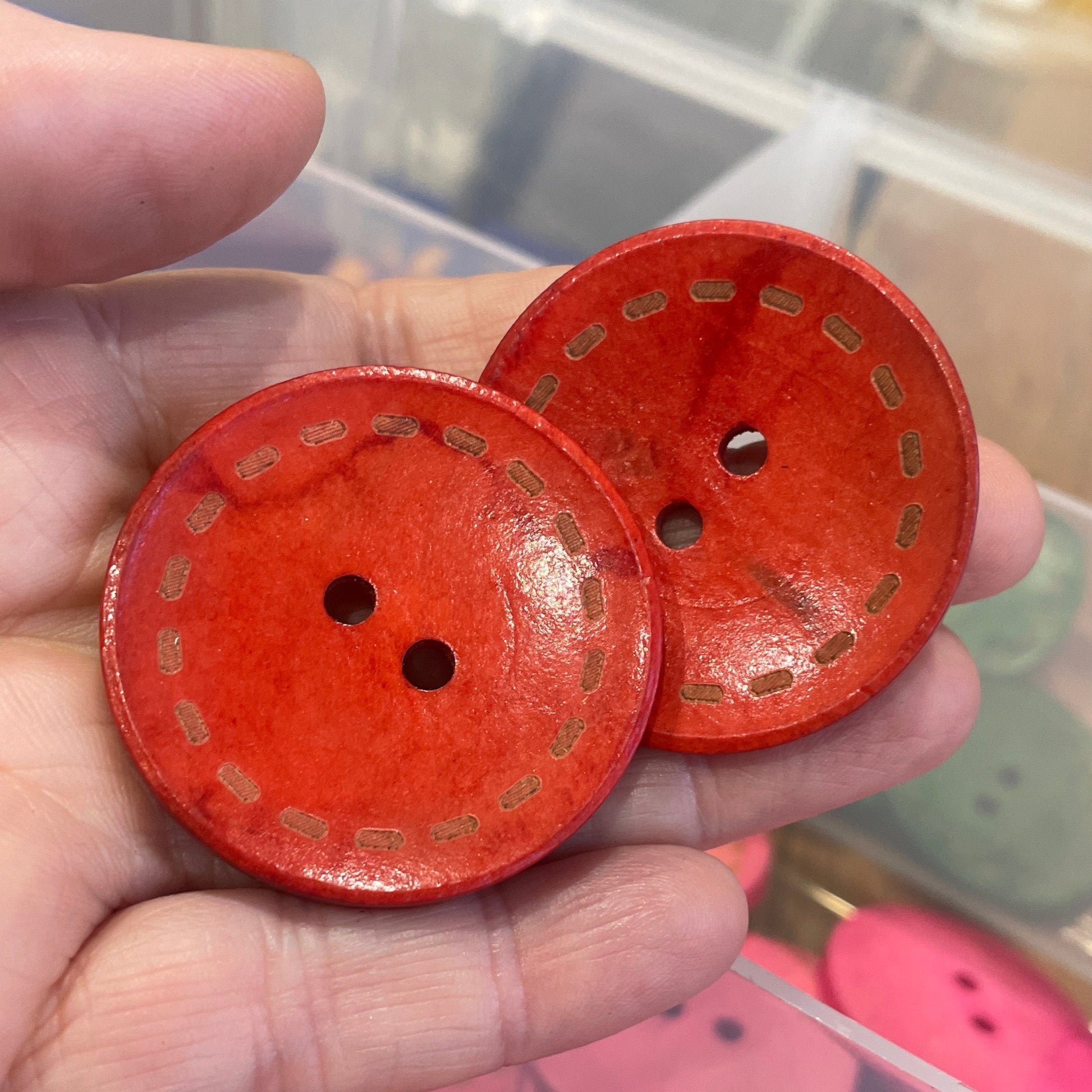 Red buttons with gold patterns held in a hand, with more buttons in the background.
