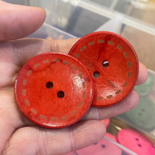 Red buttons with gold patterns held in a hand, with more buttons in the background.