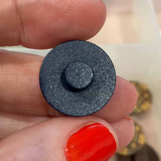 Hand holding a black button with a blurred background of a button collection box.