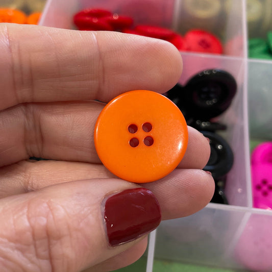 Hand holding an orange button with a background of colorful buttons in a box