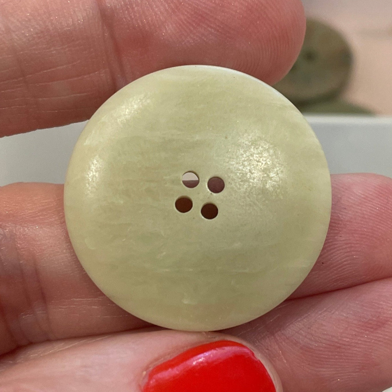 Hand holding a beige button with a clear container of buttons in the background