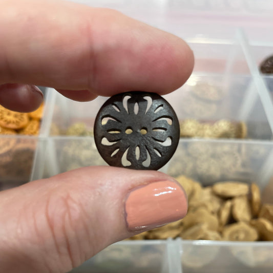 Hand holding a decorative button with a container of assorted buttons in the background