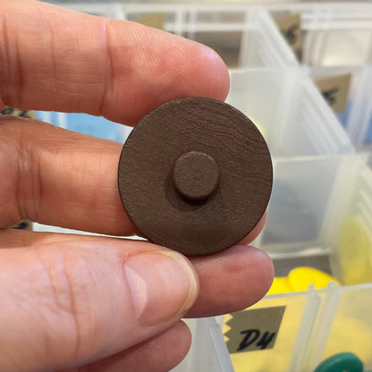 Hand holding a brown button with a container of colorful buttons in the background