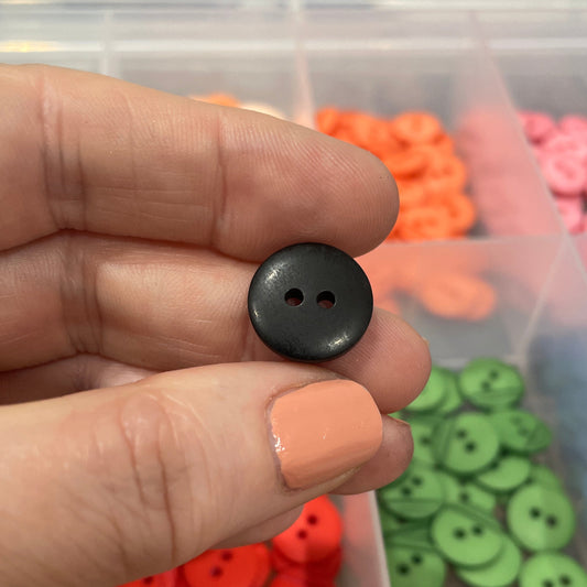 Hand holding a black button with a container of colorful buttons in the background