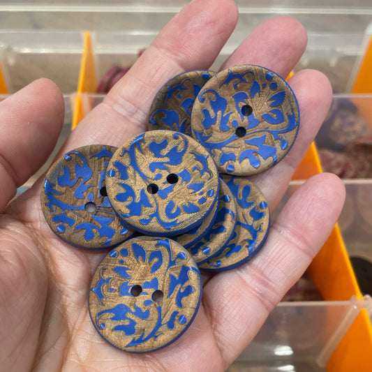 Hand holding blue and gold decorative buttons with a display box in the background.