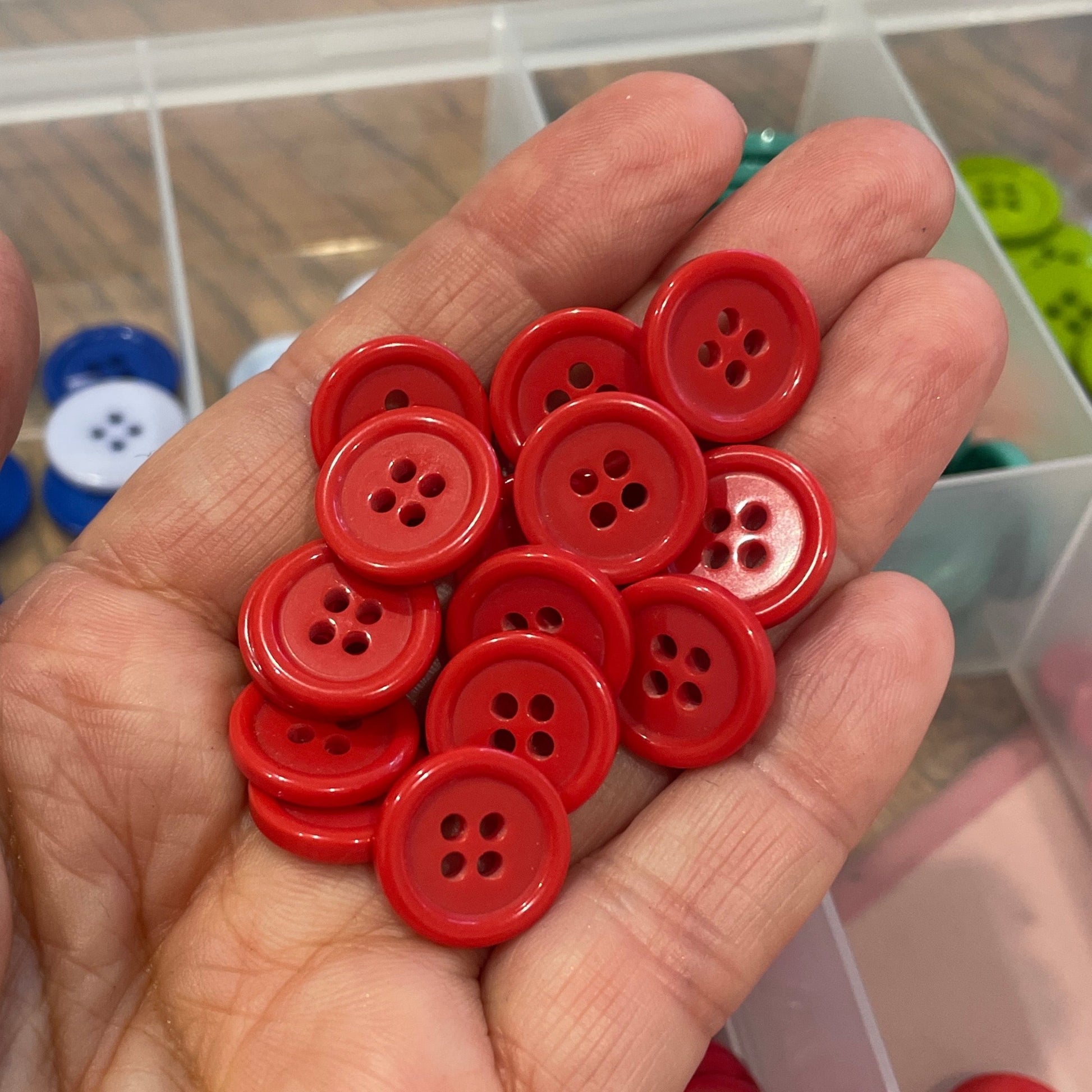 Hand holding red buttons with a container of buttons in the background