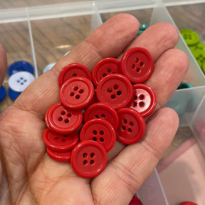 Hand holding red buttons with a container of buttons in the background