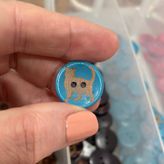 Hand holding a blue button with a design, against a background of various buttons.