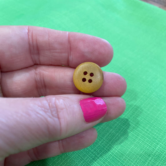 Yellow button held between fingers against a green background