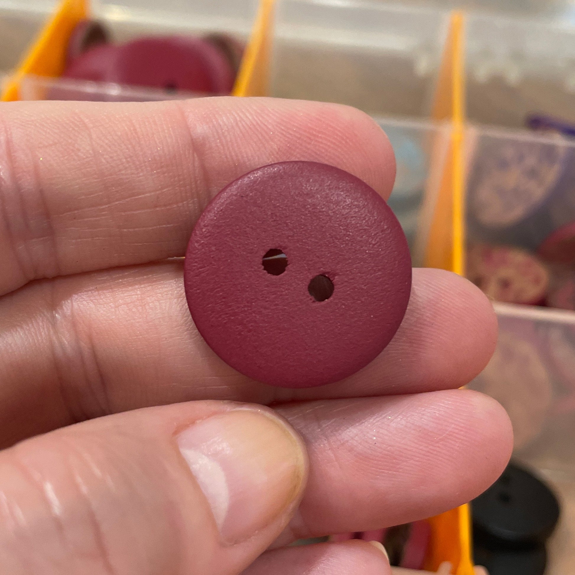 Hand holding a maroon button with a blurred background of button assortment