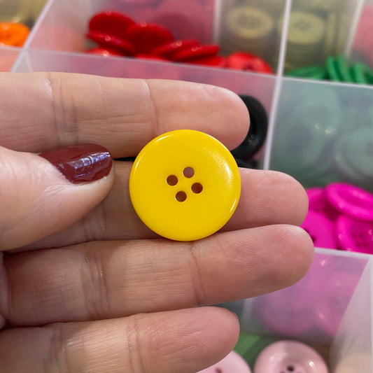 Hand holding a yellow button with a colorful button organizer in the background
