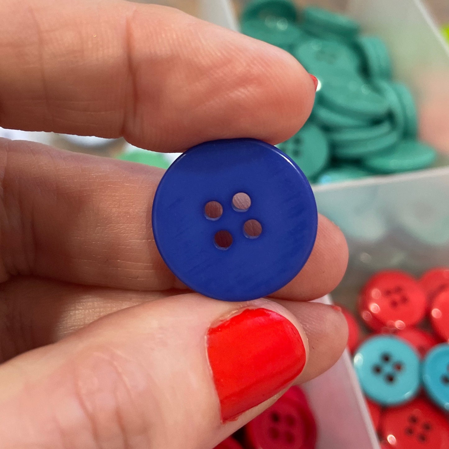 Hand holding a blue button with a container of colorful buttons in the background