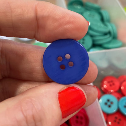 Hand holding a blue button with a container of colorful buttons in the background