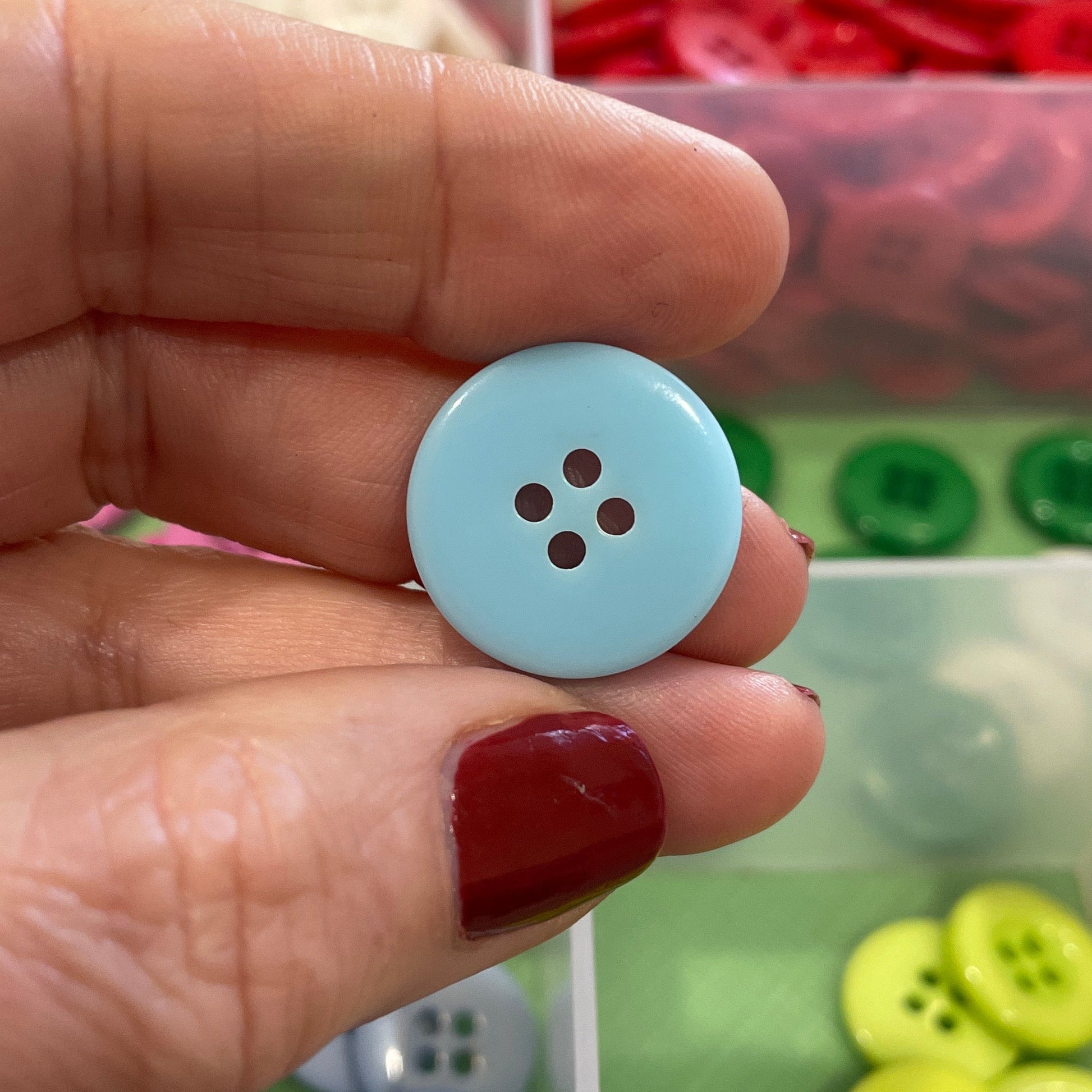 Hand holding a light blue button with a container of buttons in the background