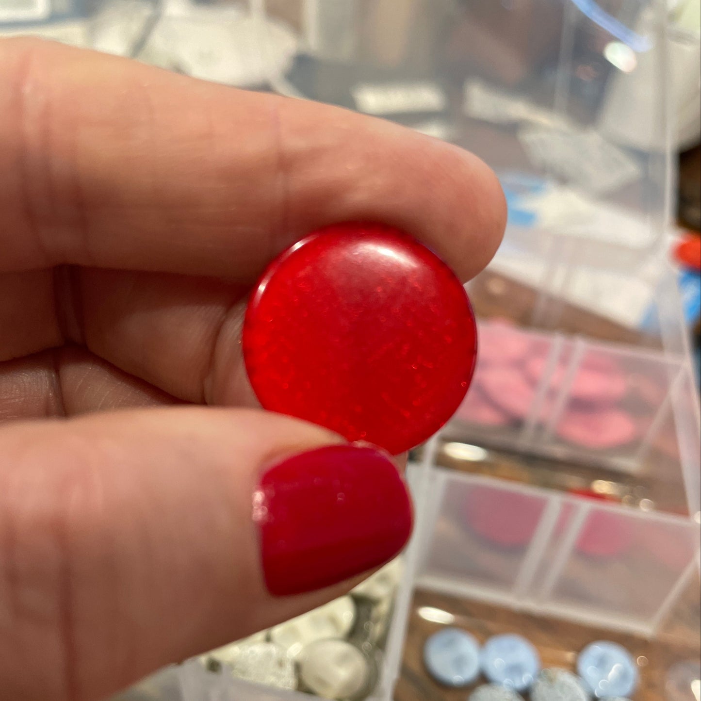 Red button held by a hand with a blurred background of a container with various buttons.