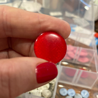 Red button held by a hand with a blurred background of a container with various buttons.