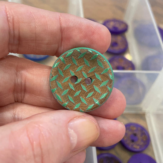 Hand holding a decorative button with a container of assorted buttons in the background.