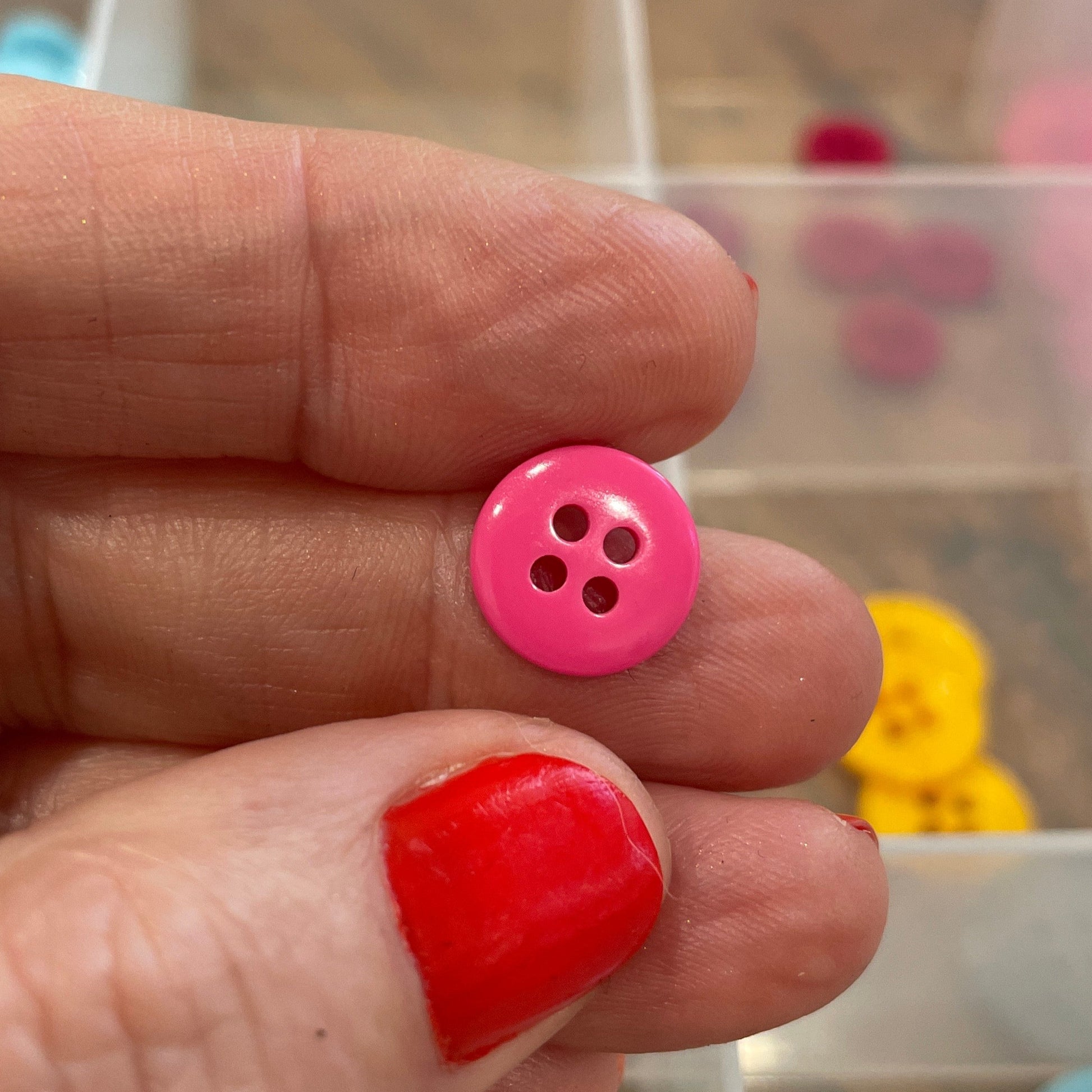 Hand holding a pink button with a blurred background of button collection