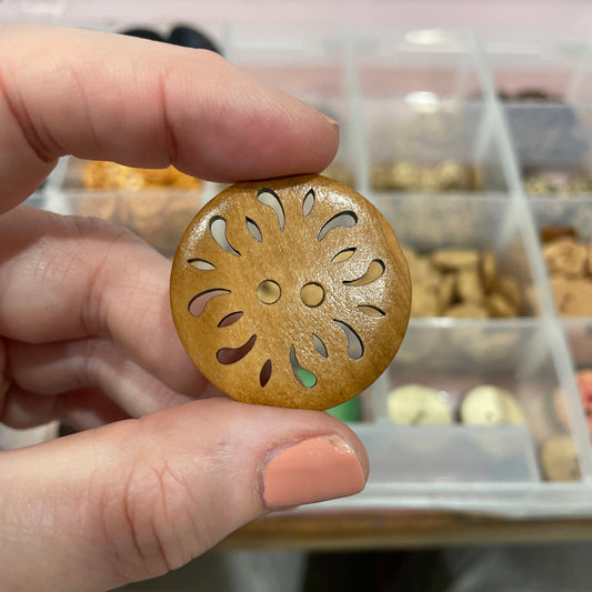 Hand holding a gold decorative object with cut-out patterns against a blurred background