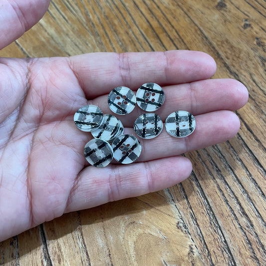 Hand holding a small collection of decorative buttons with a checkered pattern on a wooden surface.