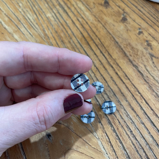 Hand holding a small round button with a pattern on a wooden surface