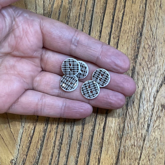 Brown and white buttons with a grid pattern held in a hand on a wooden surface