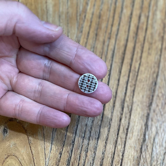 Brown and white button with a grid pattern held between fingers on a wooden surface