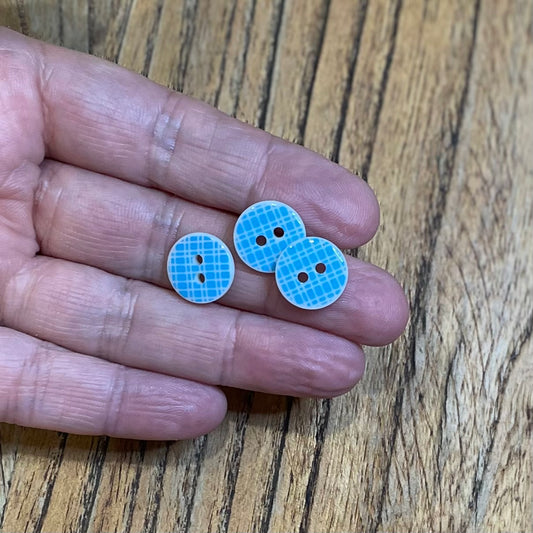 Three blue buttons held between fingers on a wooden surface