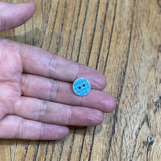 Small blue button held between fingers on a wooden surface