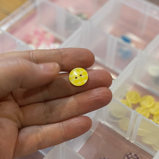 Hand holding a yellow button with a clear container of buttons in the background