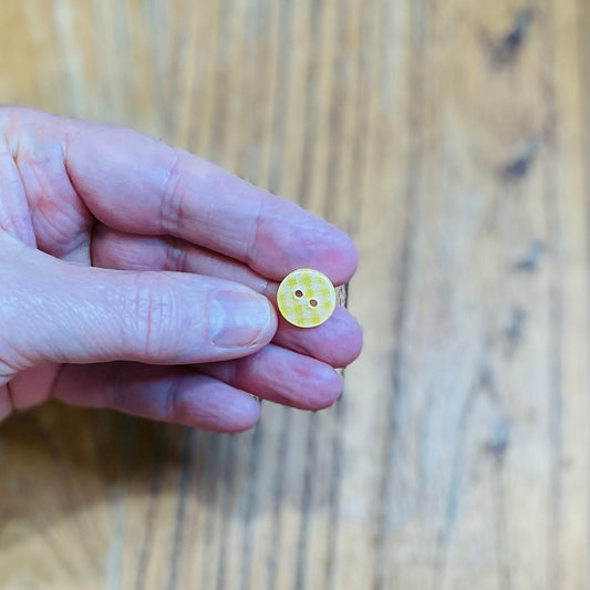 Hand holding a small yellow button with two holes on a wooden surface