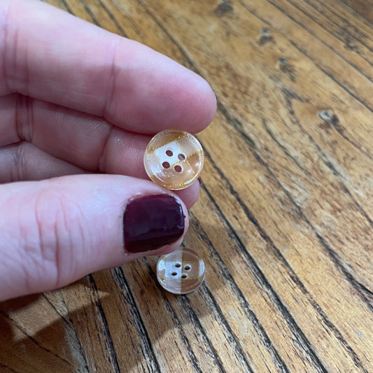 Hand holding a small brown button with four holes on a wooden surface