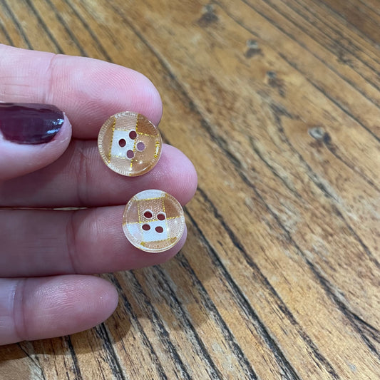 Two small round buttons held between fingers on a wooden surface