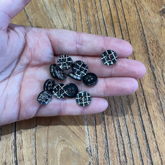 Hand holding black buttons with silver patterns on a wooden surface