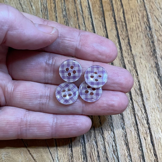 Four purple checkered buttons held between fingers on a wooden surface