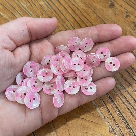 Hand holding a small pile of pink buttons on a wooden surface