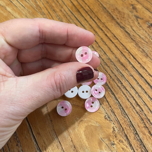 Hand holding pink buttons on a wooden surface