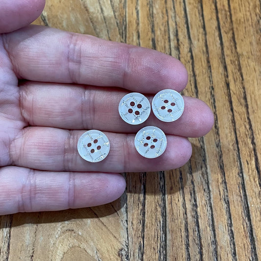 Four white buttons with four holes held between fingers on a wooden surface