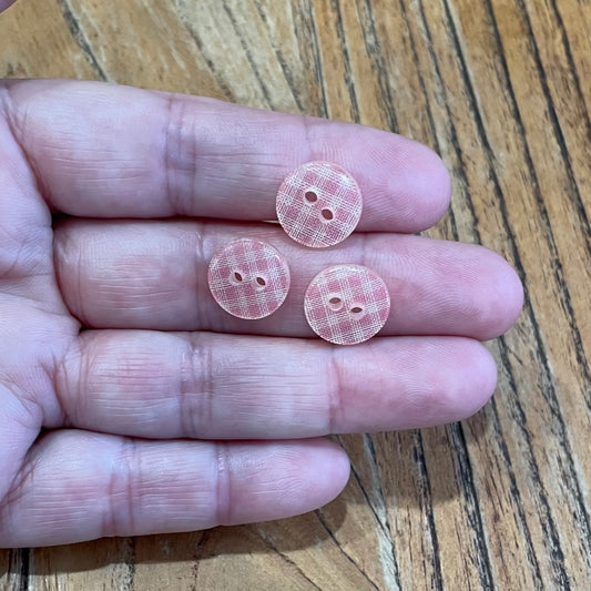 Three pink checkered buttons held between fingers on a wooden surface