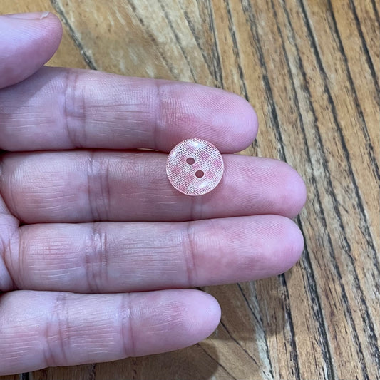 Small pink button held between fingers on a wooden surface