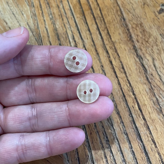 Two beige buttons held between fingers on a wooden surface