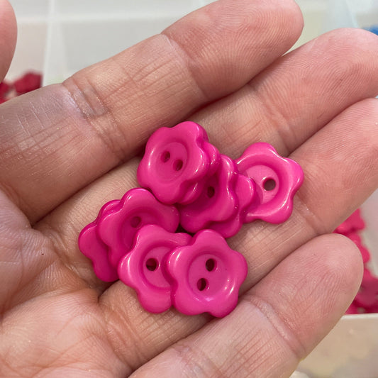 Hand holding pink buttons with a blurred background of colorful items
