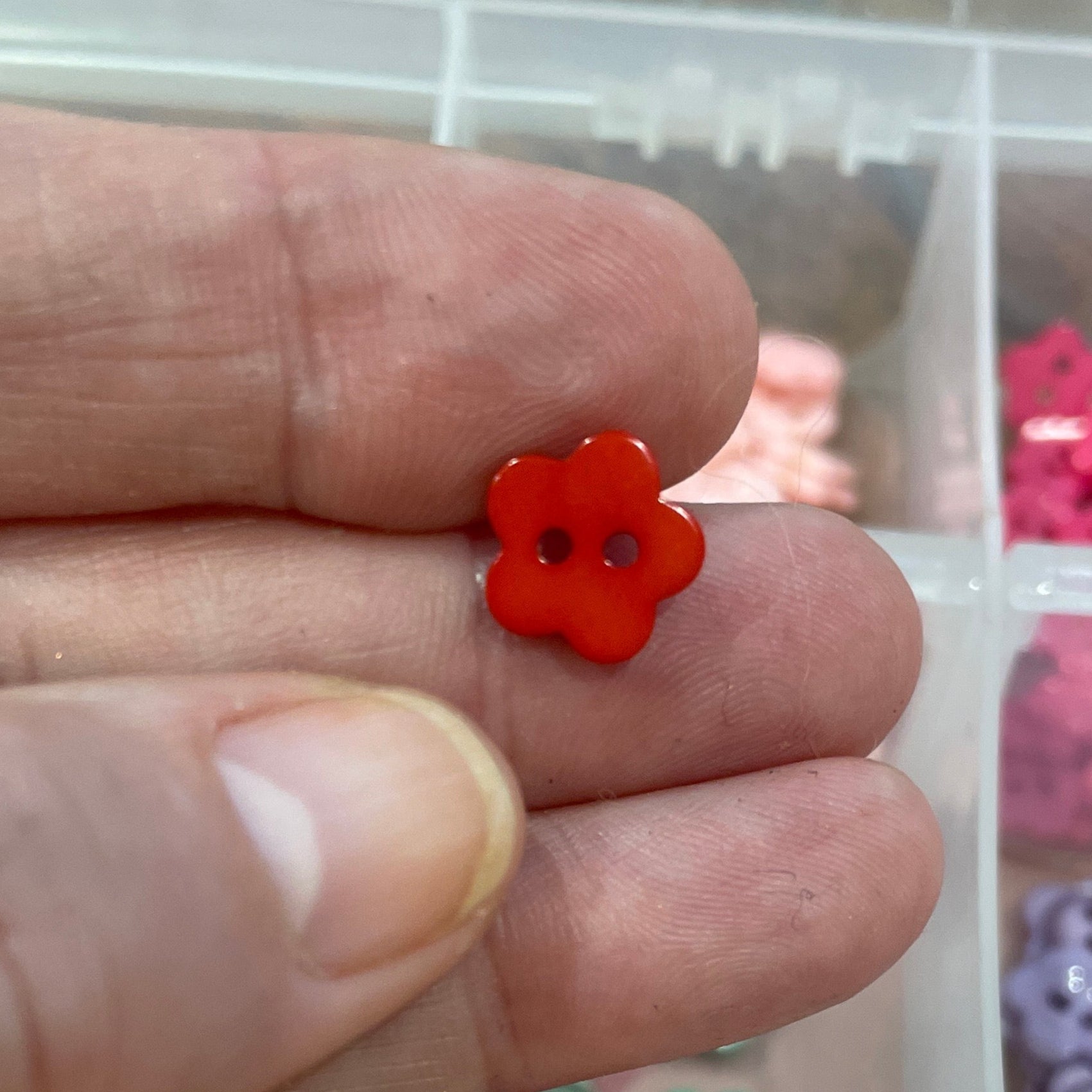Hand holding a red button with a container of various buttons in the background